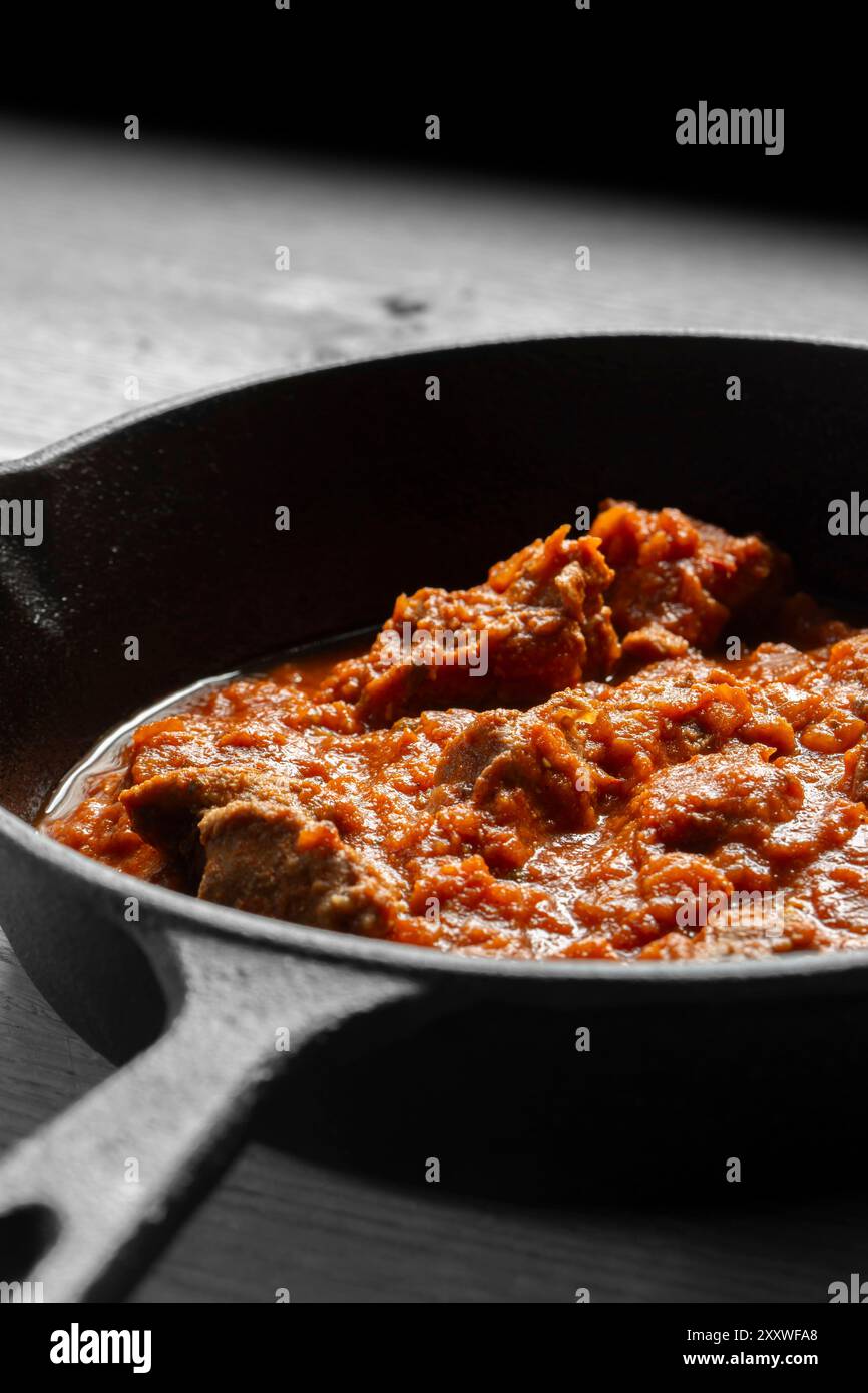 Rogan josh Lammcurry in einer gusseisernen Pfanne gekocht. Auf hölzernem Hintergrund Stockfoto
