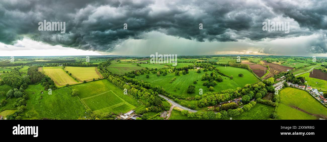 Ein mächtiges Gewitter erhebt sich über weitläufigen grünen Feldern in North Yorkshire, mit dunklen Wolken, die unter einem stimmungsvollen Himmel über der Landschaft schweben. Stockfoto