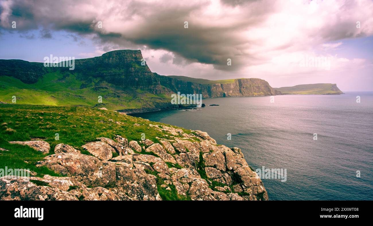 Ein atemberaubender Blick vom Neist Point aus bietet hohe Klippen vor einem Hintergrund dunkler Wolken, mit ruhigem Wasser, das das verblassende Licht reflektiert. Der Landsc Stockfoto