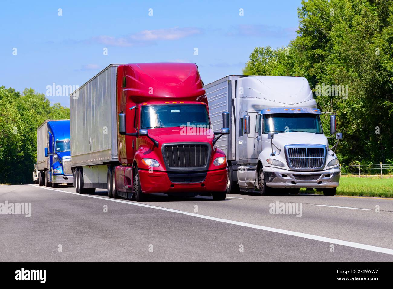 Horizontale Aufnahme von roten, weißen und blauen Trucks auf einer interstate mit Kopierraum. Hitzewellen, die aus dem heißen Asphalt steigen, erzeugen einen verschwommenen Effekt auf b Stockfoto