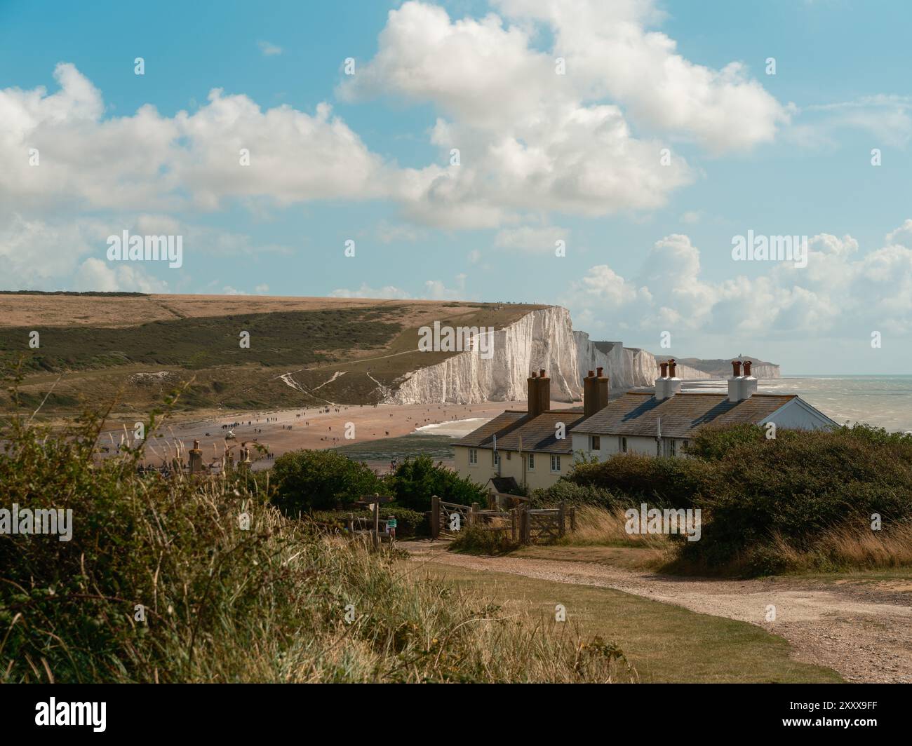 Seaford - Eastbourne - Großbritannien - 2024.08.25: Idyllische Küstenhäuser überblicken majestätische weiße Klippen vor einem hellblauen Himmel. Ein ruhiger Küstenabschnitt Stockfoto