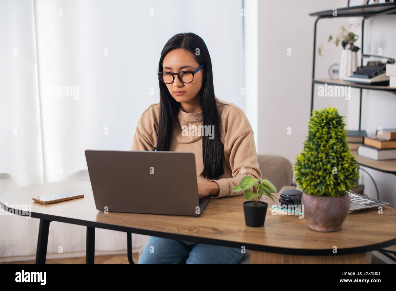 Asiatische Studentin mit Brille zu Hause sitzend, fernlernend und an einem Laptop arbeitend Stockfoto