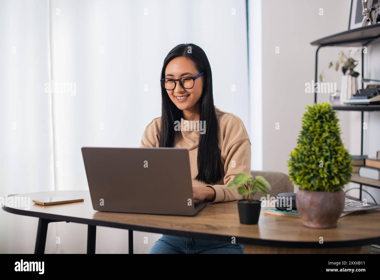 Asiatische Studentin mit Brille zu Hause sitzend, fernlernend und an einem Laptop arbeitend Stockfoto