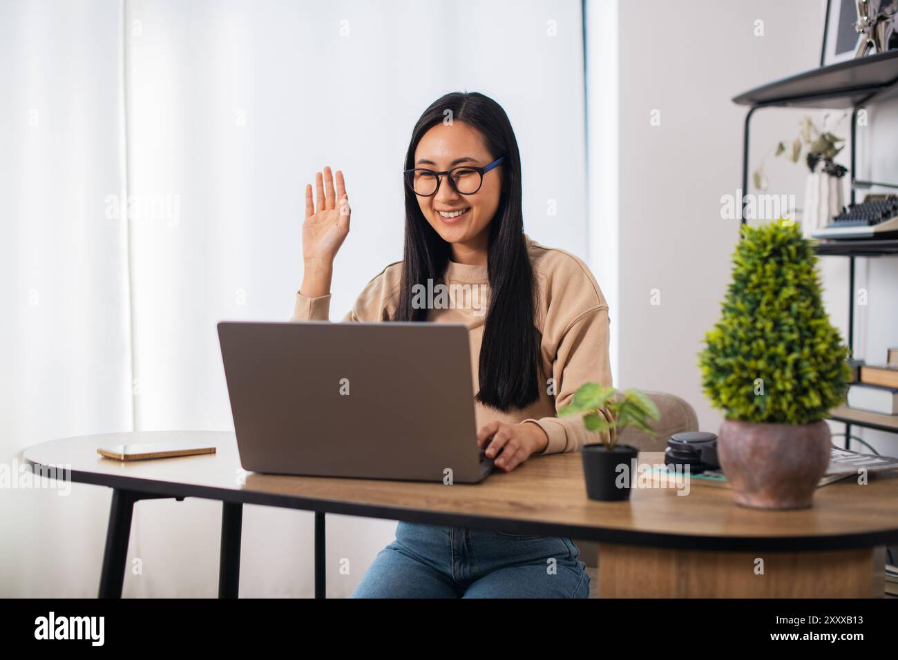 Asiatische Studentin mit Brille zu Hause sitzend, fernlernend und an einem Laptop arbeitend Stockfoto
