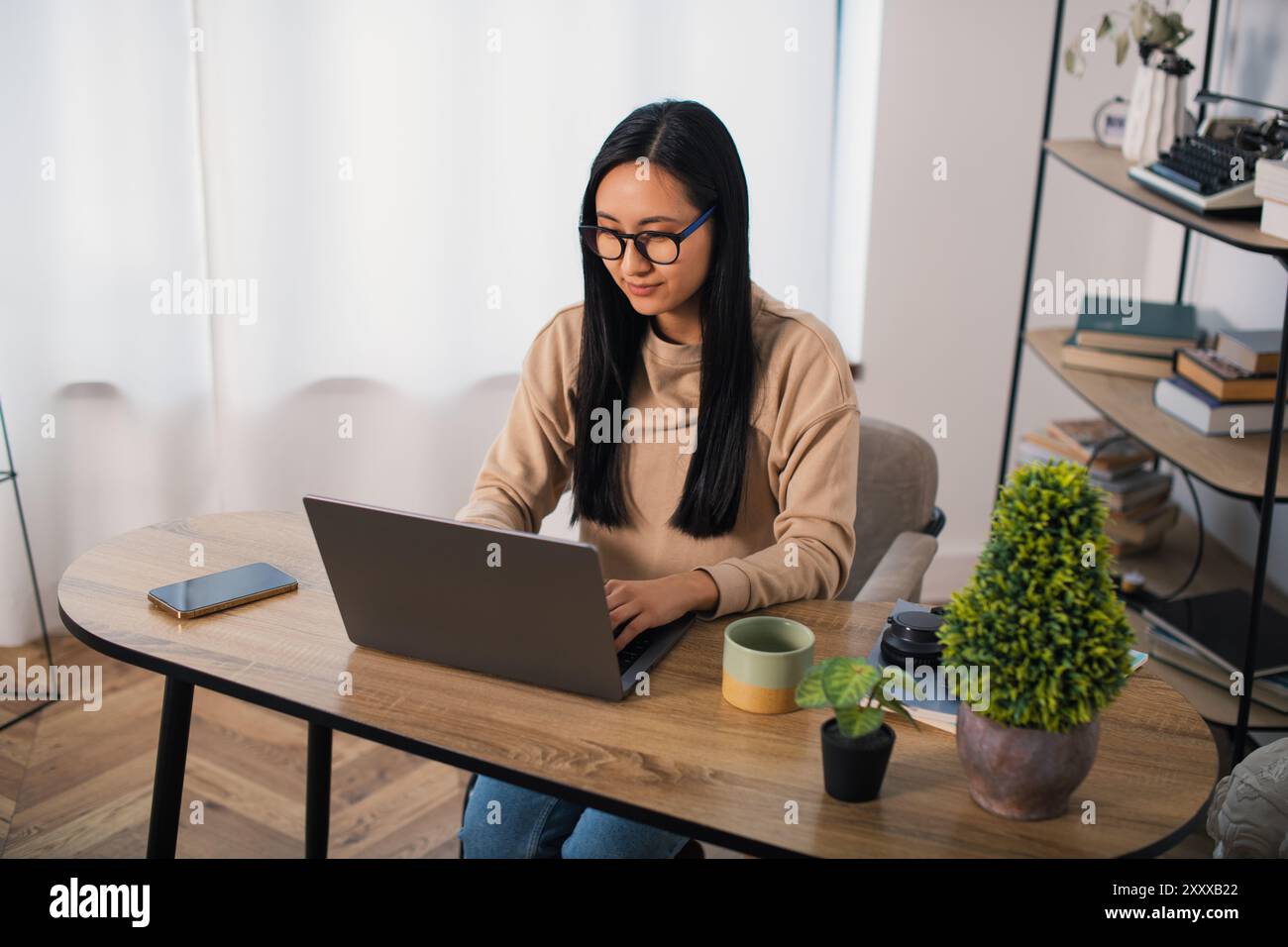 Asiatische Studentin mit Brille zu Hause sitzend, fernlernend und an einem Laptop arbeitend Stockfoto