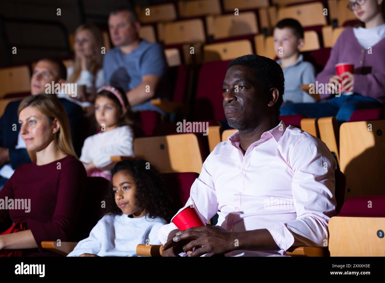 Internationale Familien essen Popcorn und sehen sich Comedy im Kinosaal an Stockfoto