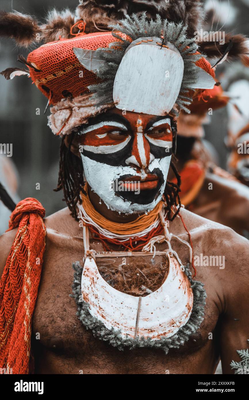 Ein Highland-Krieger von Papua-Neuguinea, Gesicht mit auffälligen Farben, einem großen gefiederten Kopfschmuck, einem Speer in der Hand und heftigen Stampfen. Stockfoto