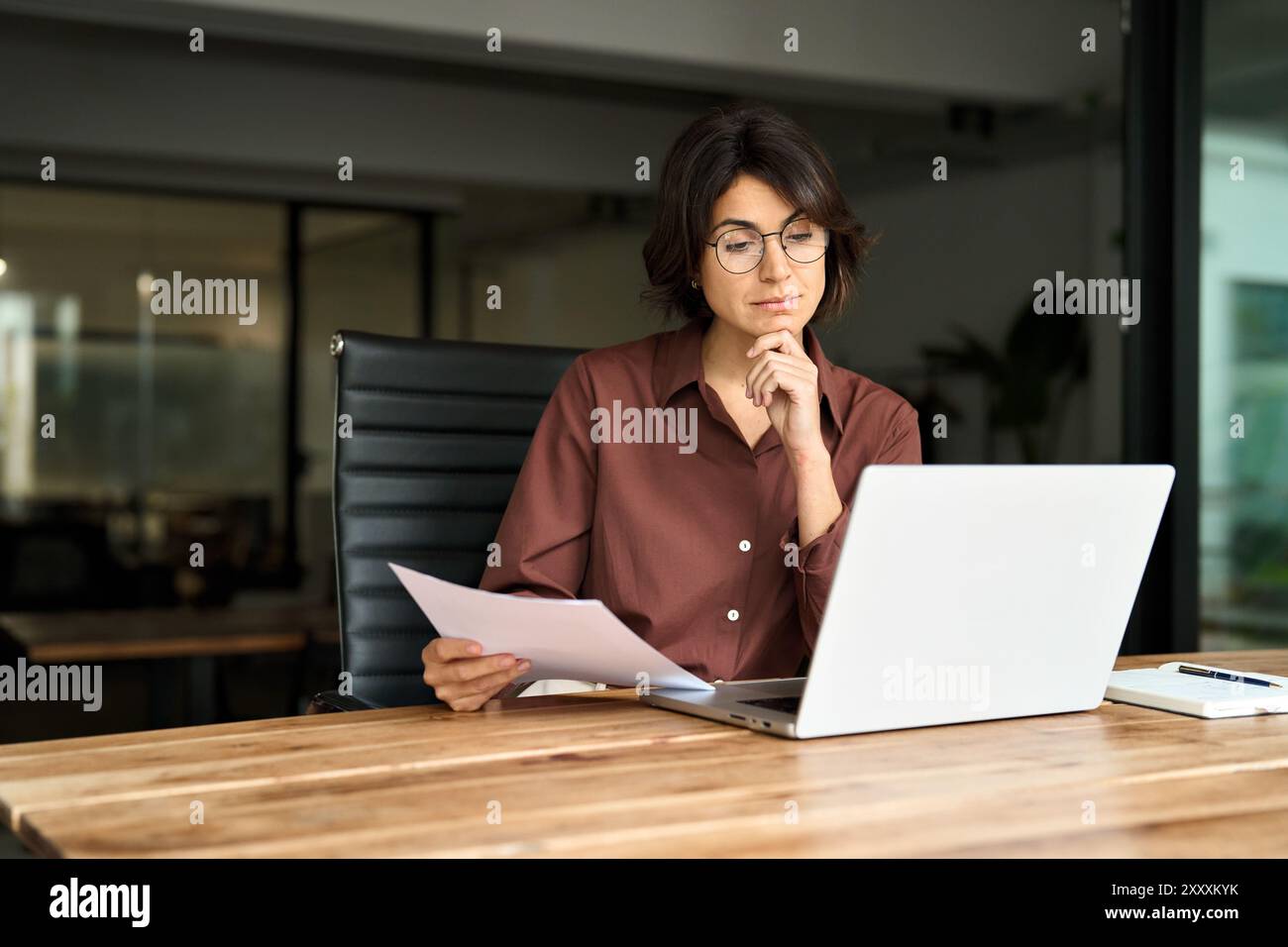 Beschäftigte junge Geschäftsfrau, die an einem Laptop arbeitet und Dokumente überprüft. Stockfoto