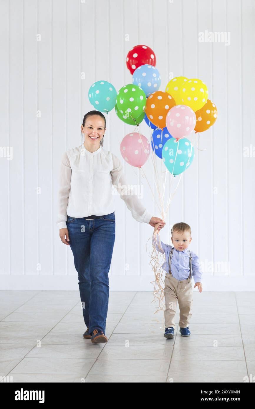 Kleiner Junge mit seiner Mutter hält eine große Reihe von bunten Luftballons Stockfoto