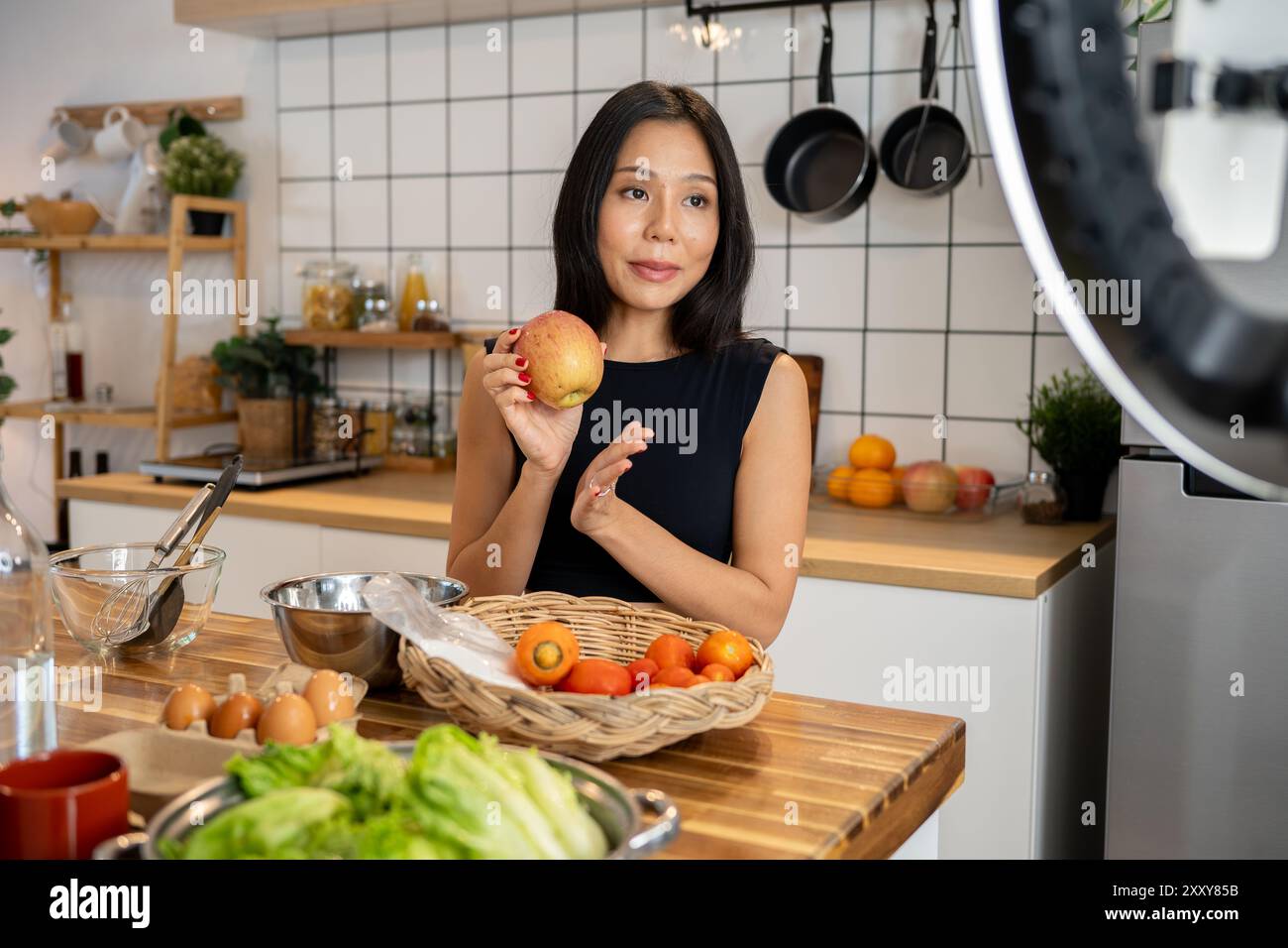 Eine attraktive asiatische Food-Bloggerin oder Content-Creatorin kocht vor der Kamera, spricht und zeigt ihre Zutaten für ein spezielles Menü Stockfoto