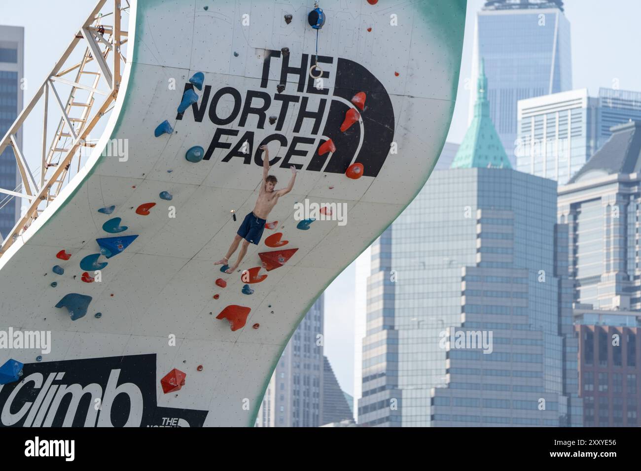 Brooklyn, Usa. August 2024. Während des North Face Climb Festivals am Pier 5 des Brooklyn Bridge Park in New York City winkt ein Kletterer den Zuschauern zu, während er mit einer Hand an der Wand festhält. Die North Face Company veranstaltete ein Climb Festival im Brooklyn Bridge Park (Foto: Derek French/SOPA Images/SIPA USA) Credit: SIPA USA/Alamy Live News Stockfoto