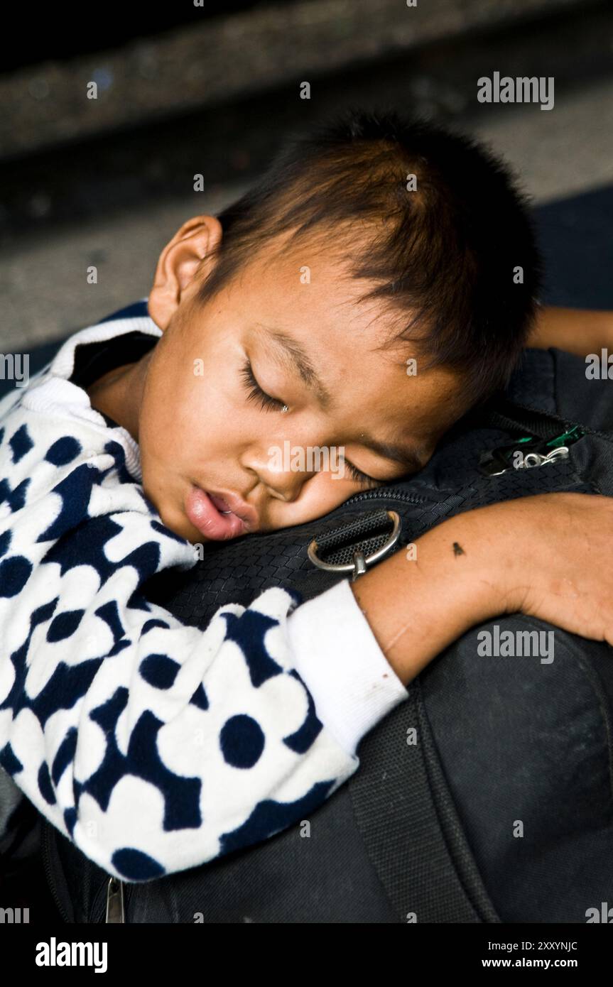 Ein süßer Thai-Junge, der auf einer großen Tasche schläft. Foto am Bahnhof in Bangkok, Thailand. Stockfoto