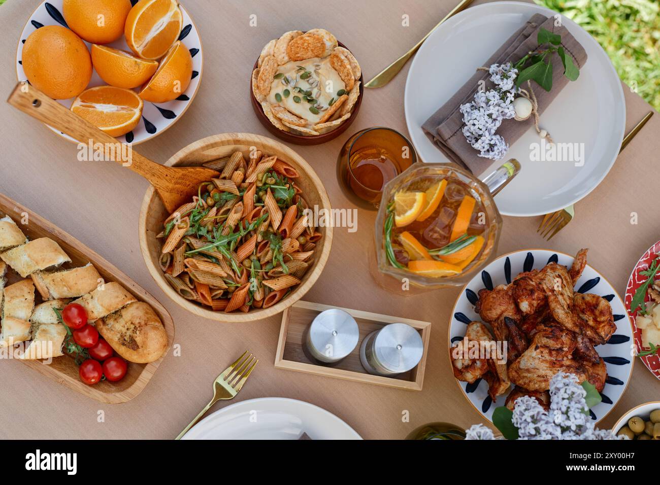 Blick von oben auf ein elegantes Speisesaal mit mediterranen Gerichten wie Pasta, Huhn, verschiedenen Brotsorten, frischem Obst und Getränken, auf einem Holztisch mit Blumen, die Charme verleihen Stockfoto