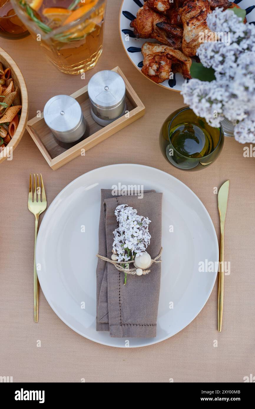 Blick von oben auf einen ordentlich angeordneten Tisch mit Tellern, Besteck, Blumen und Lebensmitteln. Verschiedene Gerichte, einschließlich Huhn und Pasta, wunderschön auf Holztisch präsentiert Stockfoto