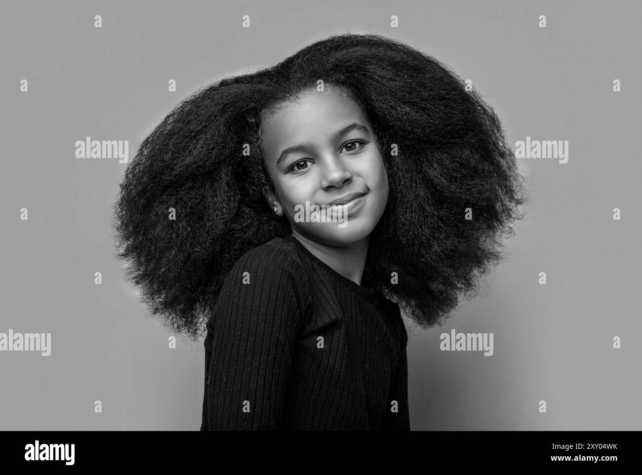 Glückliches schwarzes Teenager-Mädchen, das mit Lächeln in die Kamera schaut, lacht, Nahaufnahme Porträt. Schönes junges Afro-Mädchen. Schwarz-weiß. Stockfoto