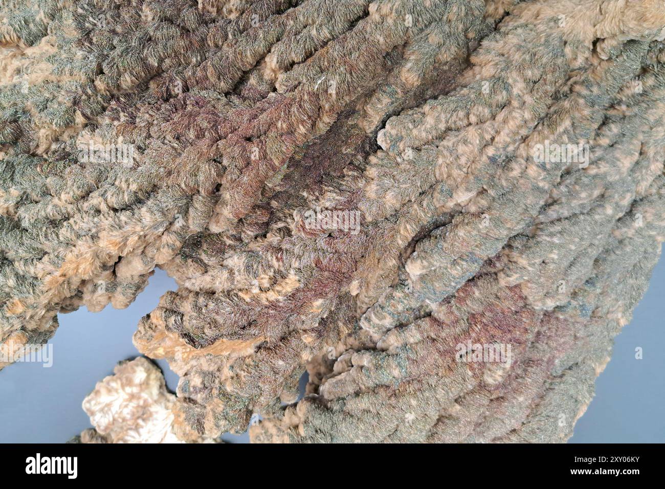 Eine raue, fasrige Mineralformation mit einer Mischung aus grünen, braunen und rötlichen Tönen, die eine strukturierte, mehrschichtige Oberfläche schafft. Stockfoto