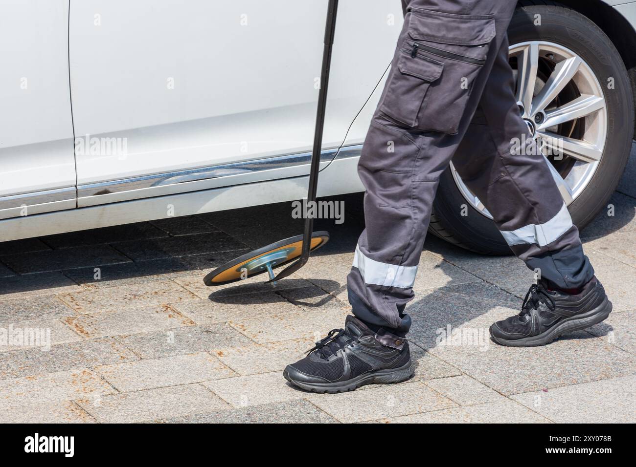 Ein Sicherheitsbeamter benutzt einen Inspektionsspiegel, um unter dem Fahrzeugboden zu überprüfen. Stockfoto
