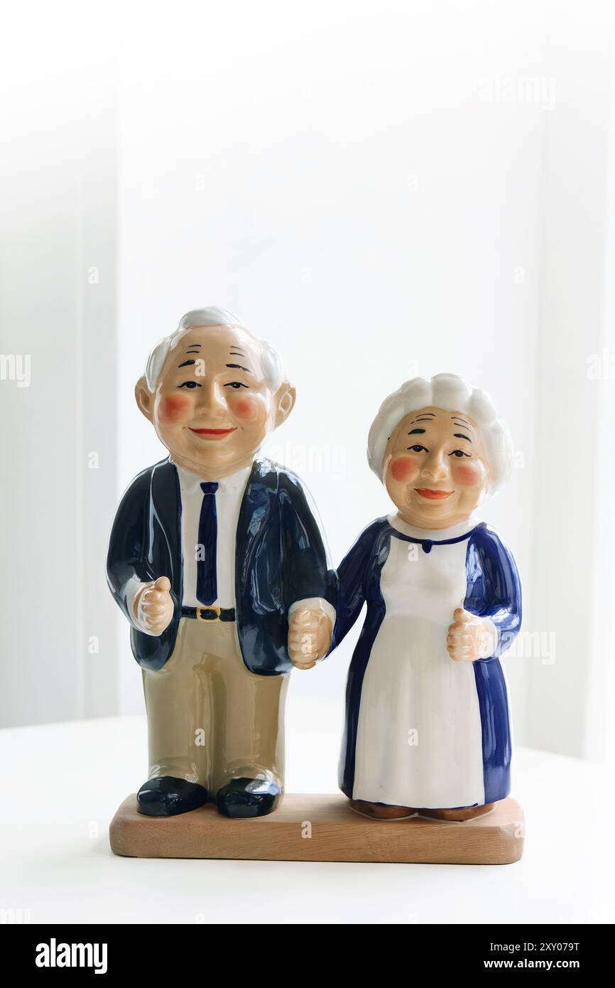 Ältere Keramikpuppen eines lächelnden Paares, das Hände hält, in Vintage-Kleidung gekleidet. Wir feiern den Internationalen Tag der älteren Menschen. Generative KI Stockfoto