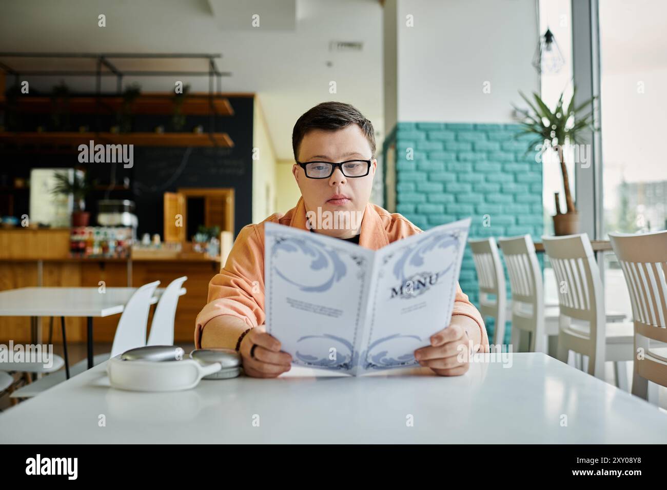 Ein Mann mit Down-Syndrom untersucht sorgfältig die Menüoptionen in einem Café und genießt ein entspannendes und inklusives Erlebnis. Stockfoto