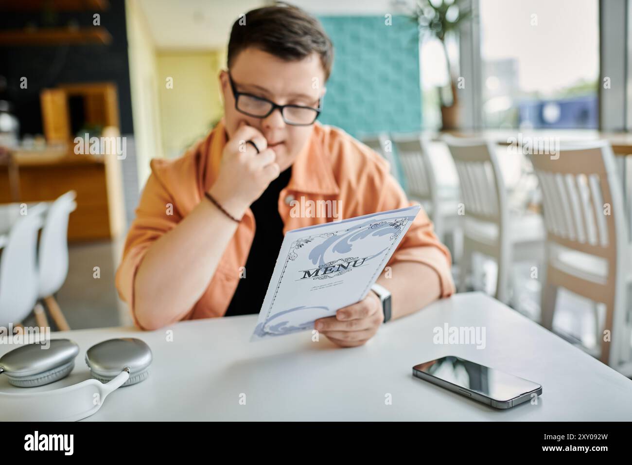 Ein Mann mit Down-Syndrom sitzt an einem Tisch in einem Café und überprüft die Speisekarte sorgfältig. Stockfoto