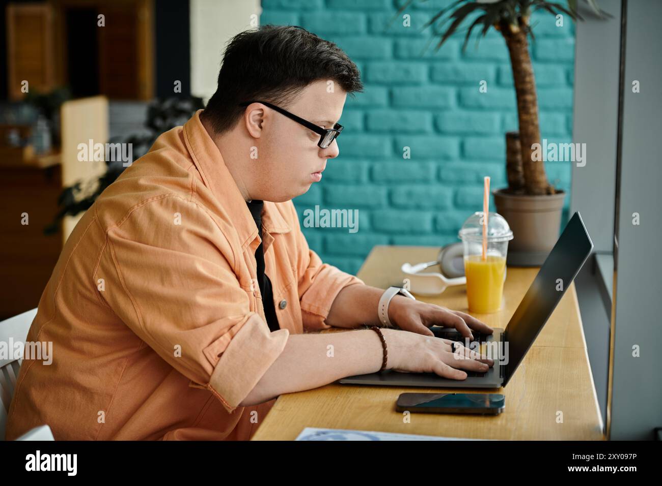 Ein Mann mit Down-Syndrom arbeitet in einem Café an seinem Laptop. Stockfoto