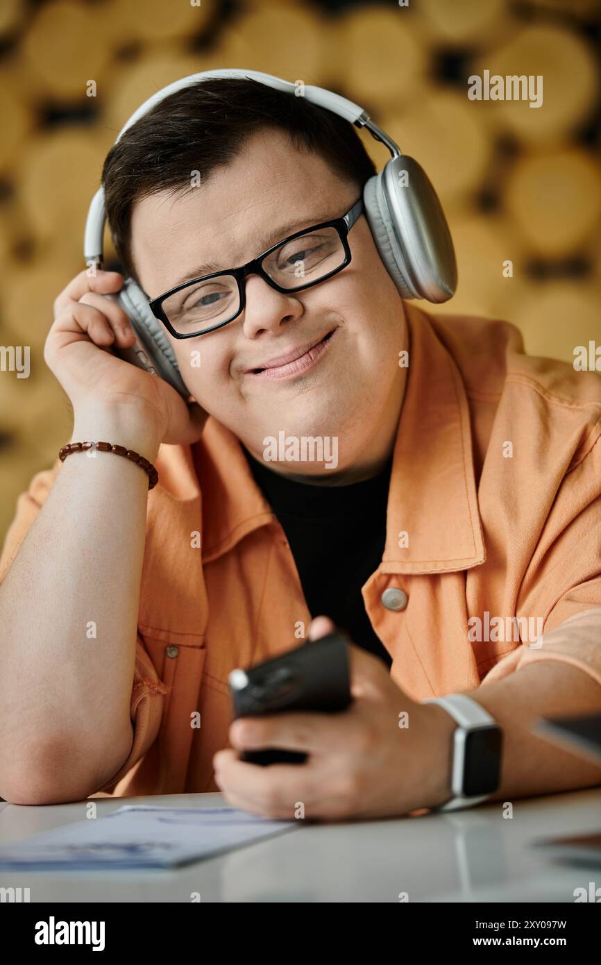 Ein Mann mit Down-Syndrom arbeitet ferngesteuert an seinem Telefon, während er Kopfhörer in einem Café trägt. Stockfoto