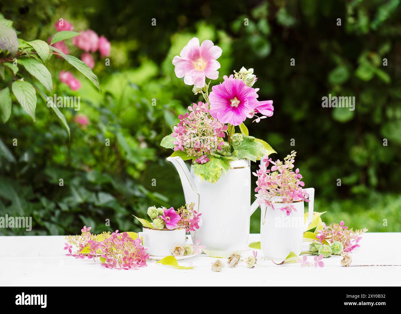 Wunderschöner Strauß aus rosa, magentafarbenen Hollyhock und lila Hortensie Blumen in einer weißen Vintage Porzellan Teekanne auf dem Tisch. (Alcea rosea) Cottage gart Stockfoto