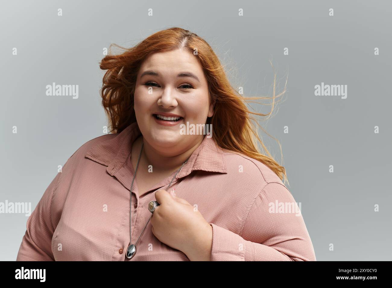 Eine große Frau mit rotem Haar lächelt selbstbewusst, ihr windgeblasenes Haar verleiht dem Bild mehr Bewegung. Stockfoto
