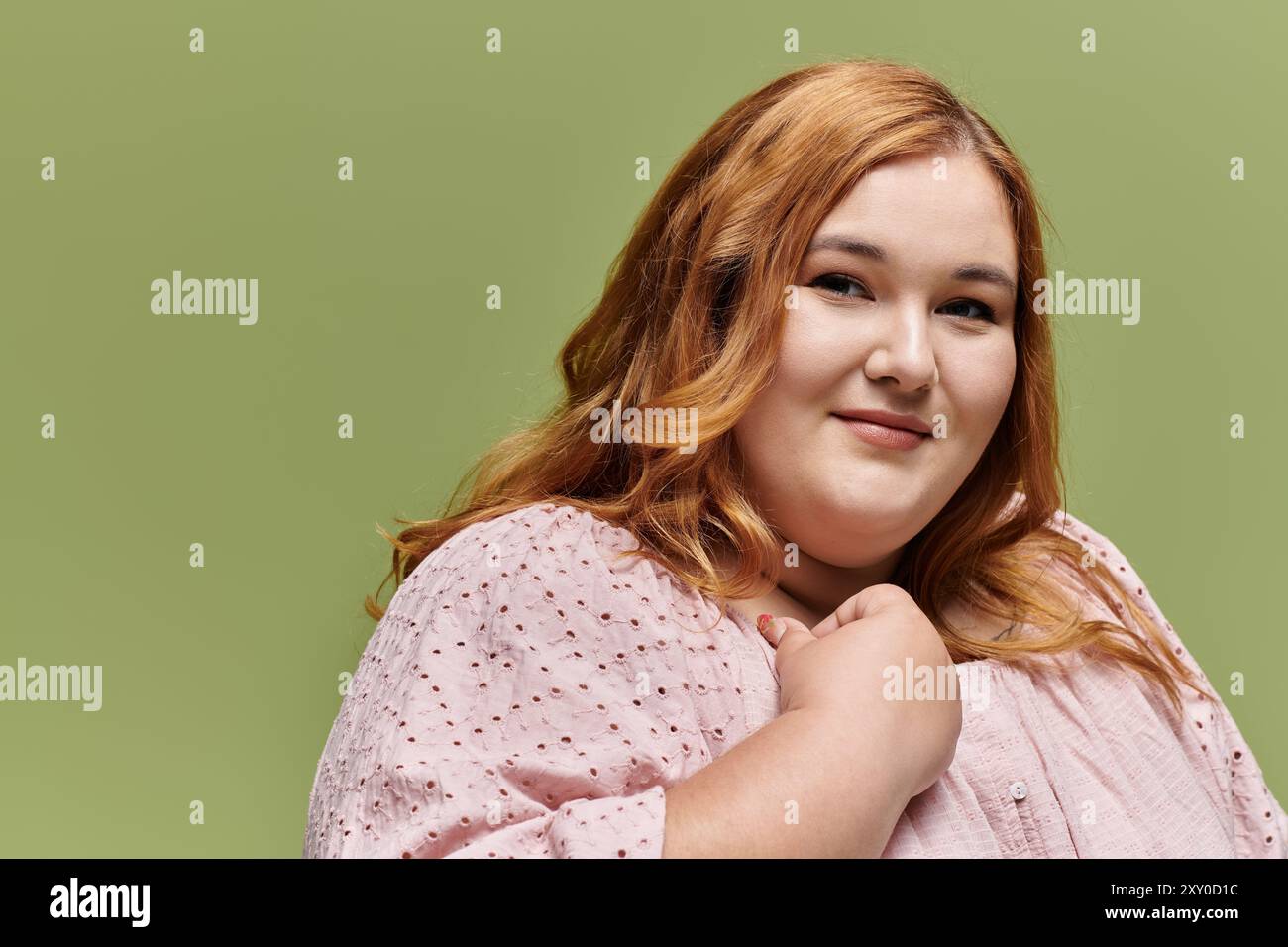 Eine Frau mit langen roten Haaren lächelt sanft in die Kamera und trägt ein hellrosa Oberteil. Stockfoto