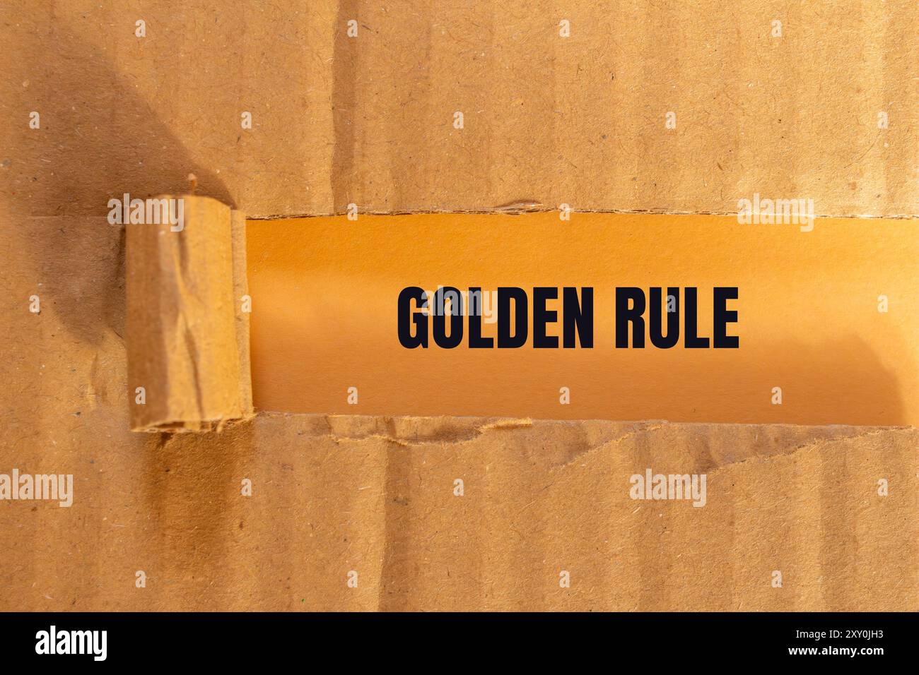 Goldene Regelnachricht auf zerrissenem Papppapier mit orangem Hintergrund. Konzeptionelles goldenes Regelsymbol. Kopierbereich. Stockfoto