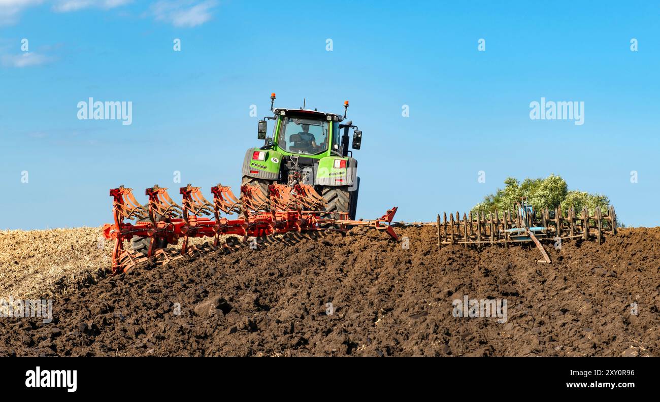 Traktor mit 7-Blatt-Umkehrpflug und Packer auf dem Feld, nach der Getreideernte - 2139 Stockfoto