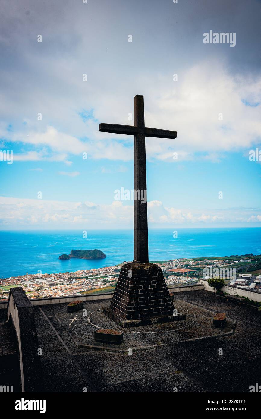 Ein markantes Kreuz steht hoch vor dem Hintergrund des azurblauen Atlantiks und der üppigen grünen Landschaft der Azoren, dieses malerische Aussichtspunkt, unter dem Sie gefangen gehalten werden Stockfoto