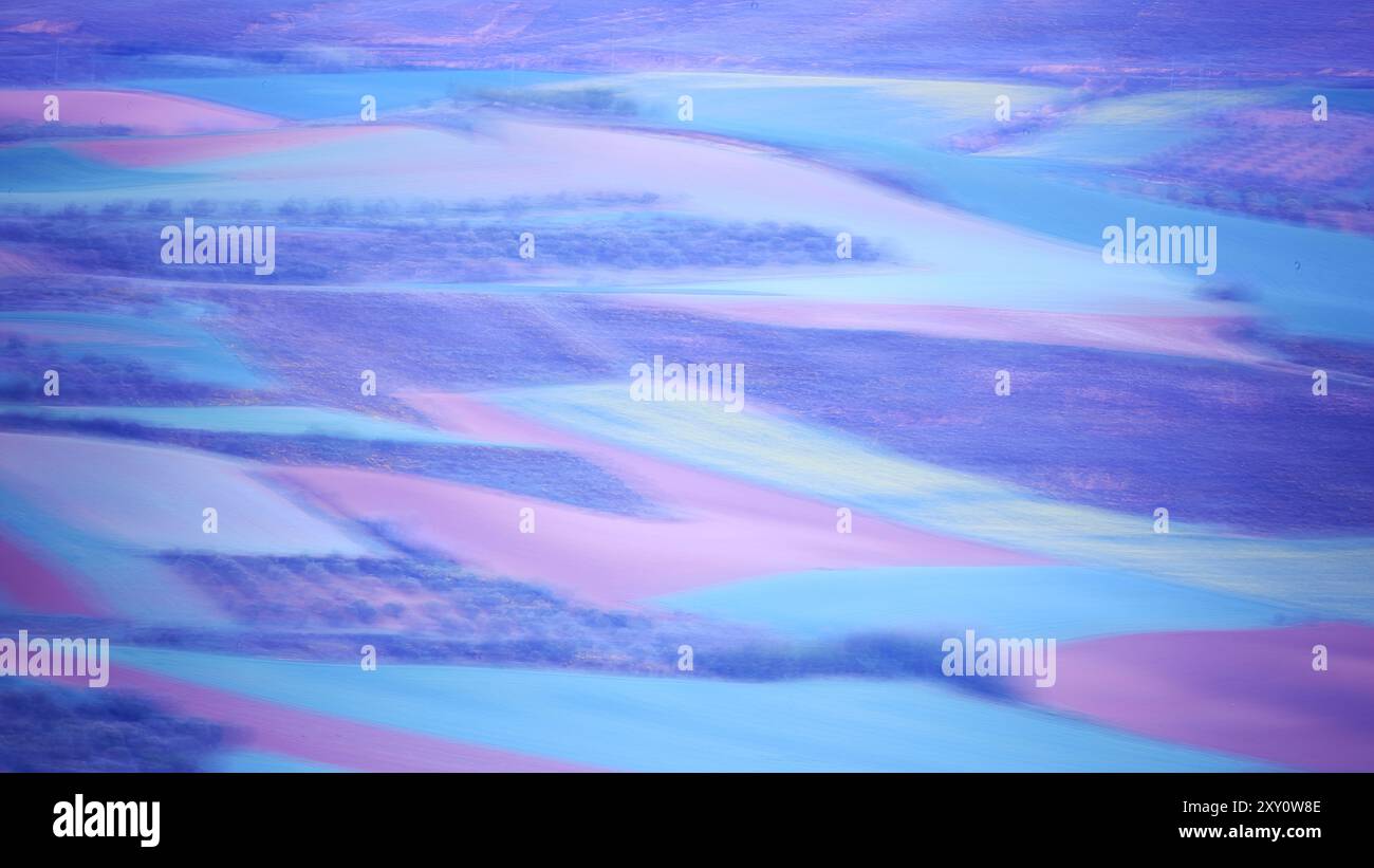 Ein atemberaubendes abstraktes Luftbild, das Bauernfelder zeigt, die mit surrealen Lila-, Blau- und Rosa-Tönen bemalt sind und eine ätherische Landschaft schafft Stockfoto