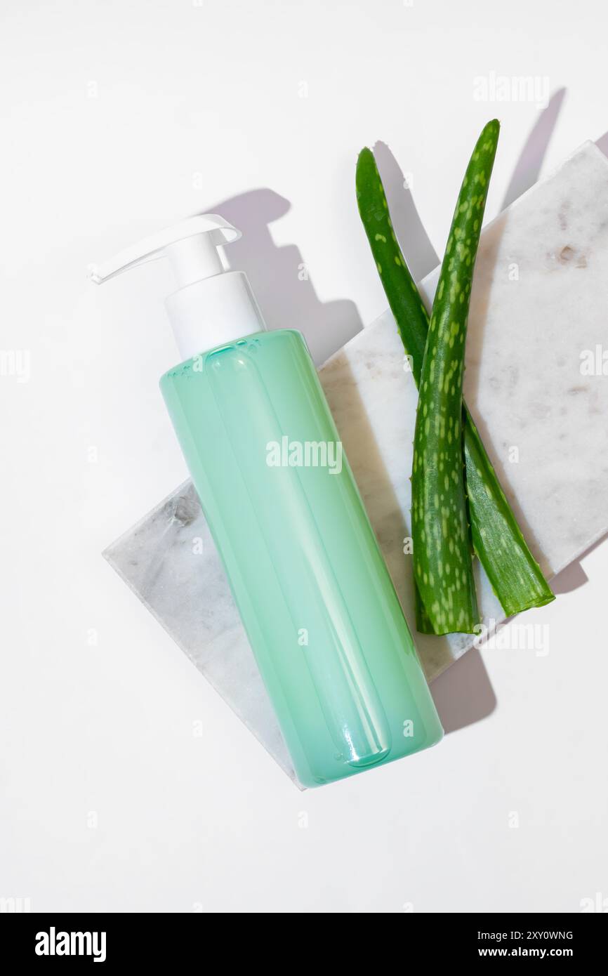 Eine elegante Flasche Aloe Vera Gel kombiniert mit frischen Aloe-Scheiben auf einer eleganten Marmorplatte, die ein sauberes und biologisches Kosmetikthema darstellt Stockfoto
