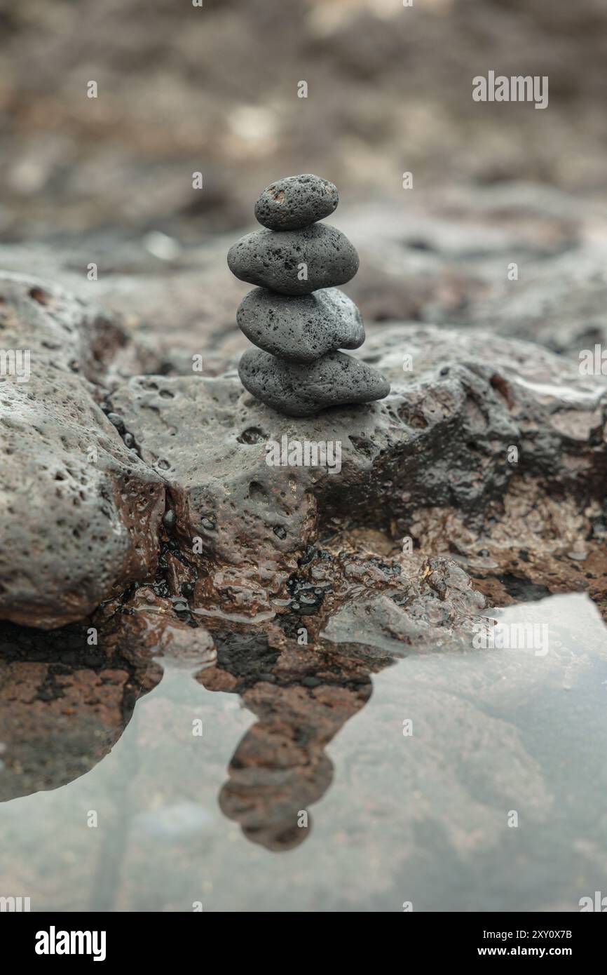 Friedliche Szene aus Zen-Steinen, die sorgfältig in einem Stapel auf einer zerklüfteten felsigen Oberfläche neben einer reflektierenden Wasserpfütze balanciert sind, die Ruhe und balan vermitteln Stockfoto