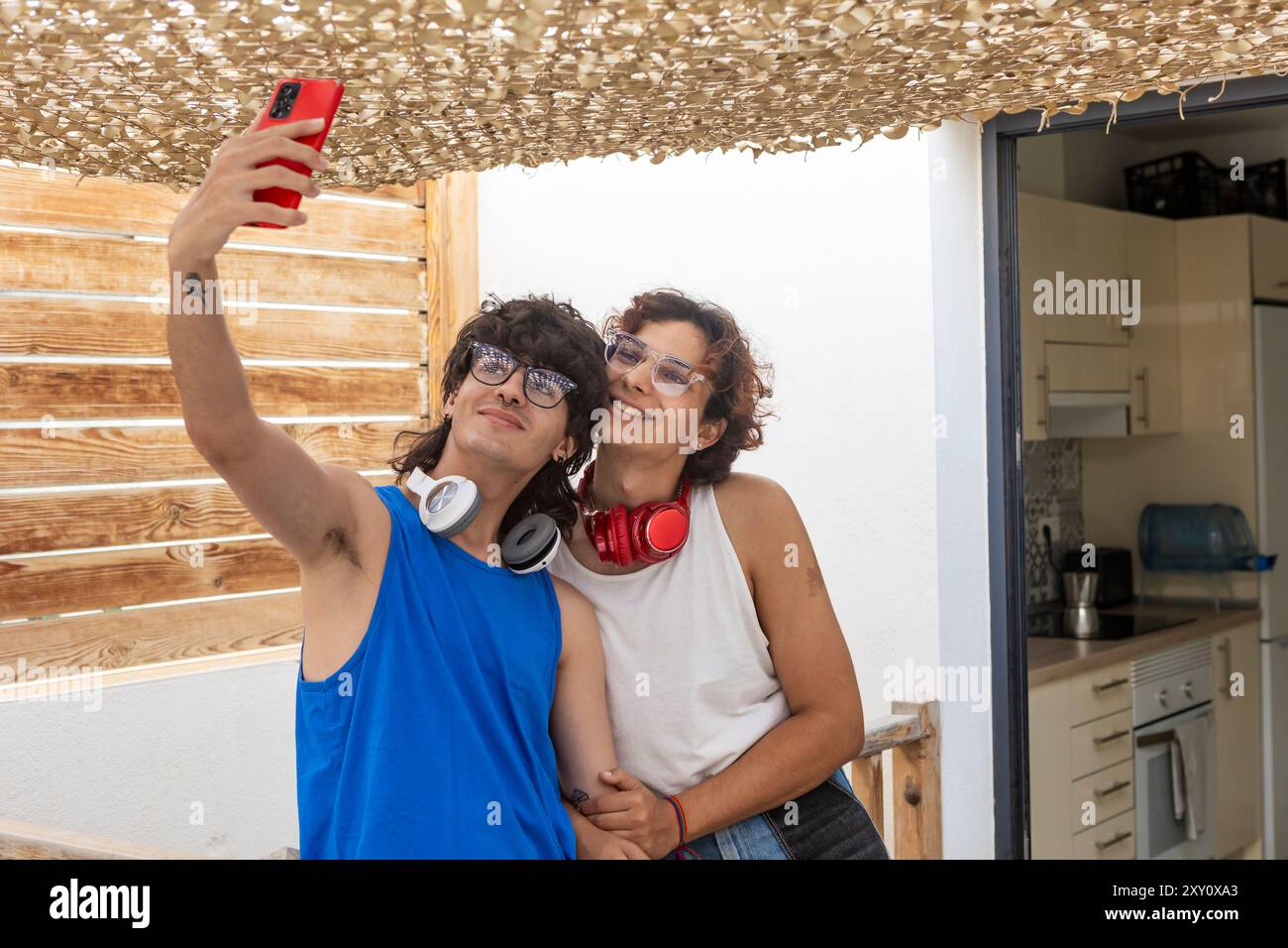 Ein fröhliches schwules Paar fängt gemeinsam ein Selfie ein und teilt einen gemütlichen Moment in der Tür zu Hause, umgeben von natürlichem Licht und zwangloser Inneneinrichtung Stockfoto