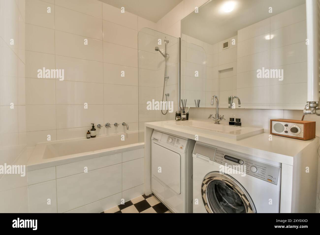 Ein modernes Badezimmer mit eingebauter Badewanne, Waschbecken, Spiegel und praktischer Waschmaschine im Zimmer. Stockfoto