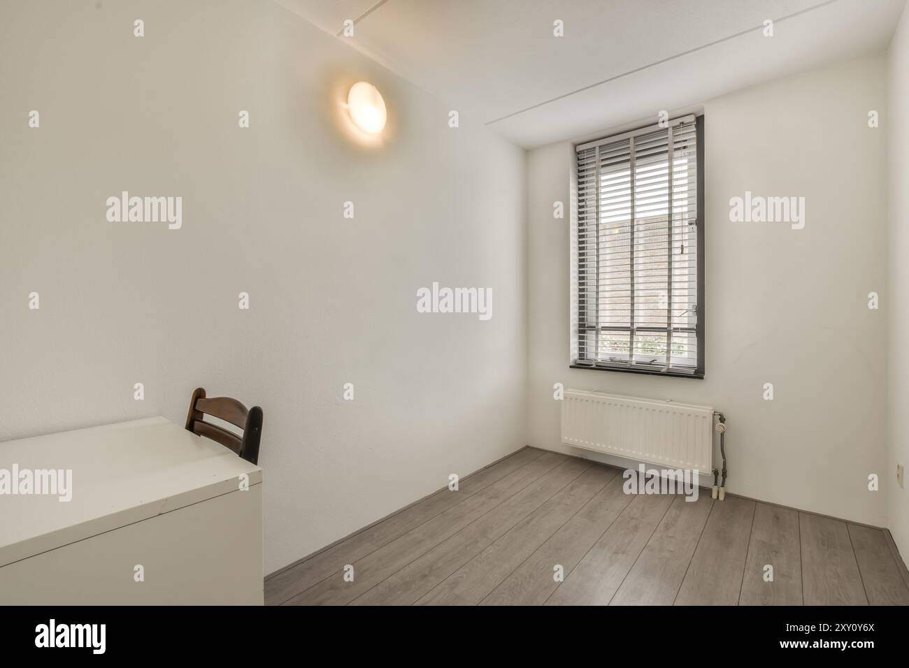 Ein einfaches, kleines Schlafzimmer mit einem Einzelbett, Laminatboden und einem Fenster mit Jalousien für natürliches Licht. Stockfoto