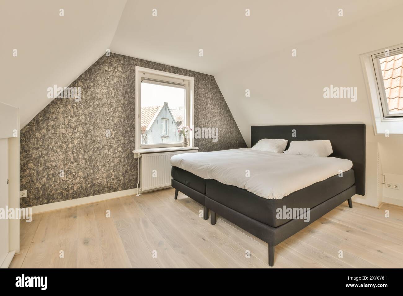 Modernes Schlafzimmer im Dachgeschoss mit einem komfortablen schwarzen Bett, schicken gemusterten Tapeten und einem von Tageslicht beleuchteten Holzboden. Stockfoto