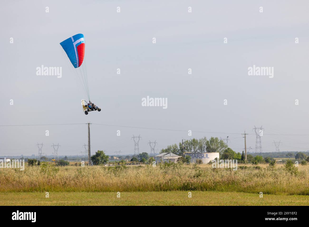 Motorisiertes Gleitschirmfliegen über ein Feld mit Stromkabeln. Stockfoto
