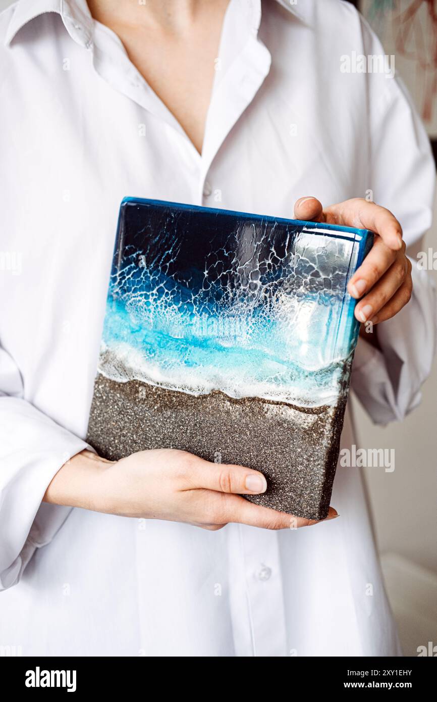 Nahaufnahme einer Person, die ein Kunstwerk aus Kunstharz im Ozean hält, das detailgetreue Handwerkskunst und einzigartiges Design zeigt. Handgefertigte Wohnkultur im Küstenstil. Stockfoto