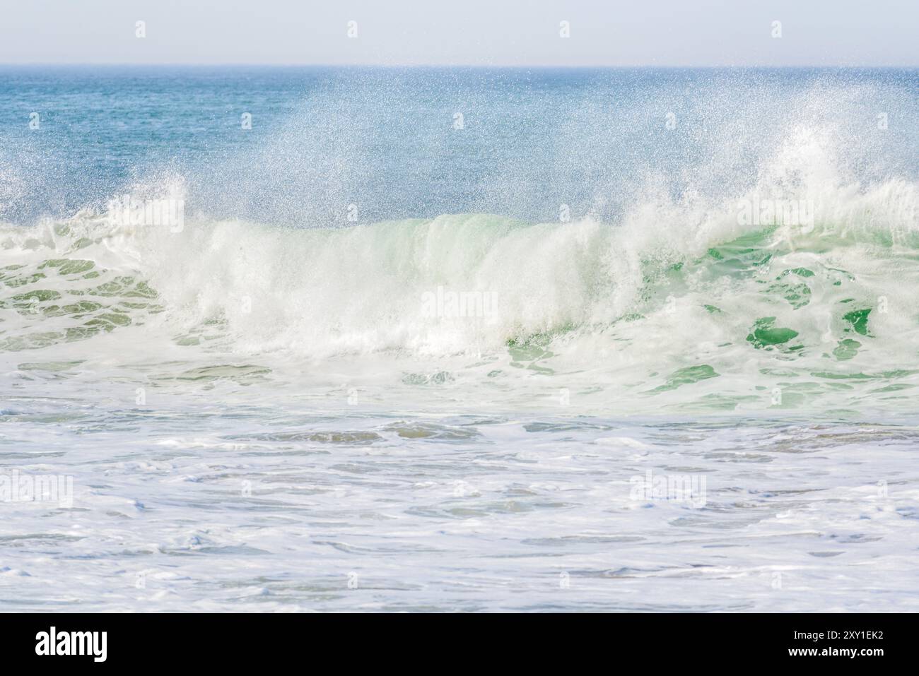 Vorderansicht einer großen Meereswelle, die am Ufer bricht und an einem windigen Tag Sprühwolken aufwirft Stockfoto
