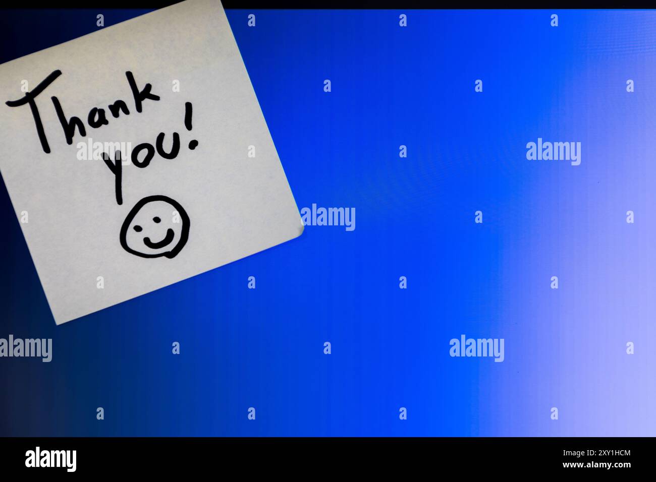 Ein Dankeschön mit einem Smiley-Gesicht darauf. Die Notiz befindet sich auf einem blauen Hintergrund mit einer schweren Vignette Stockfoto