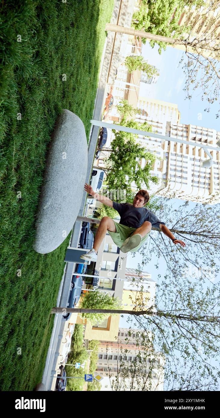 Er springt über großen Stein, ein junger sportlicher Mann zeigt sportliche Agilität und führt dynamische Bewegungen während des Parkour-Trainings im öffentlichen Park durch Stockfoto