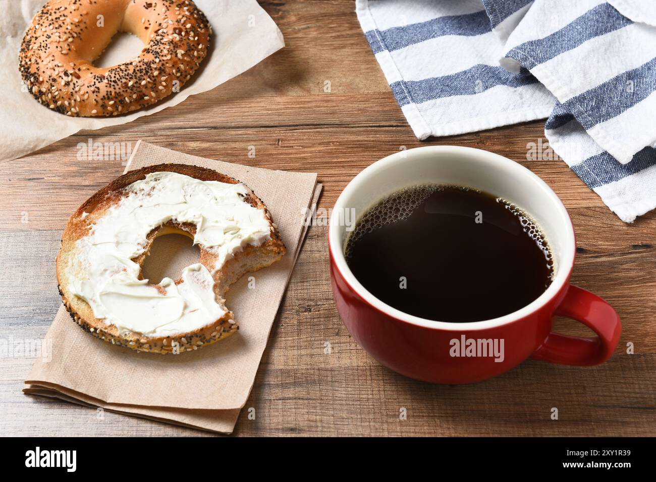 Eine frische Tasse Kaffee und ein Bagel mit Frischkäse auf einem Holztisch. Stockfoto