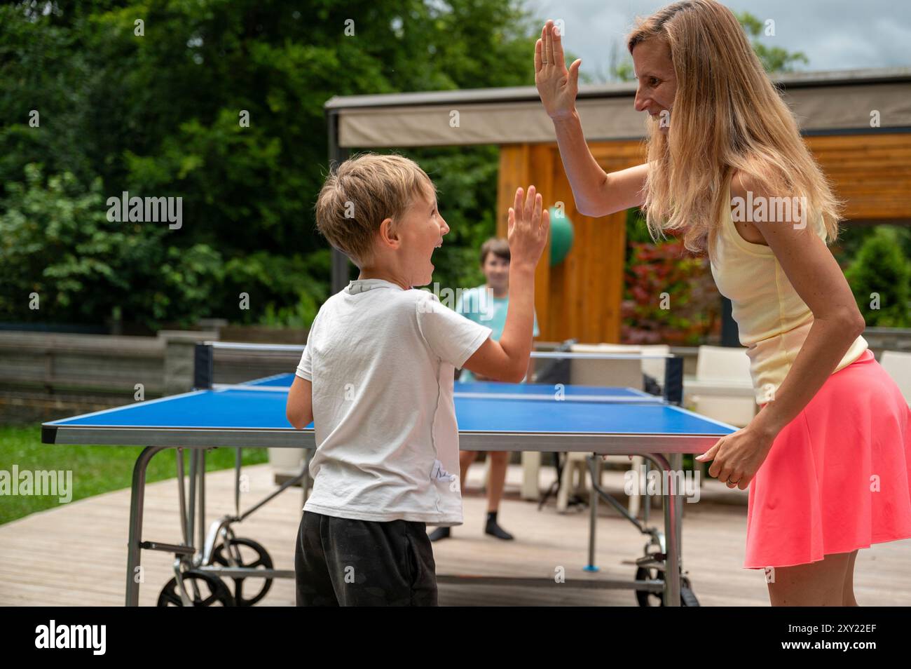 Die junge Mutter jubelte ihren kleinen Sohn, der Tischtennis spielt, und gab ihm einen High Five. Stockfoto
