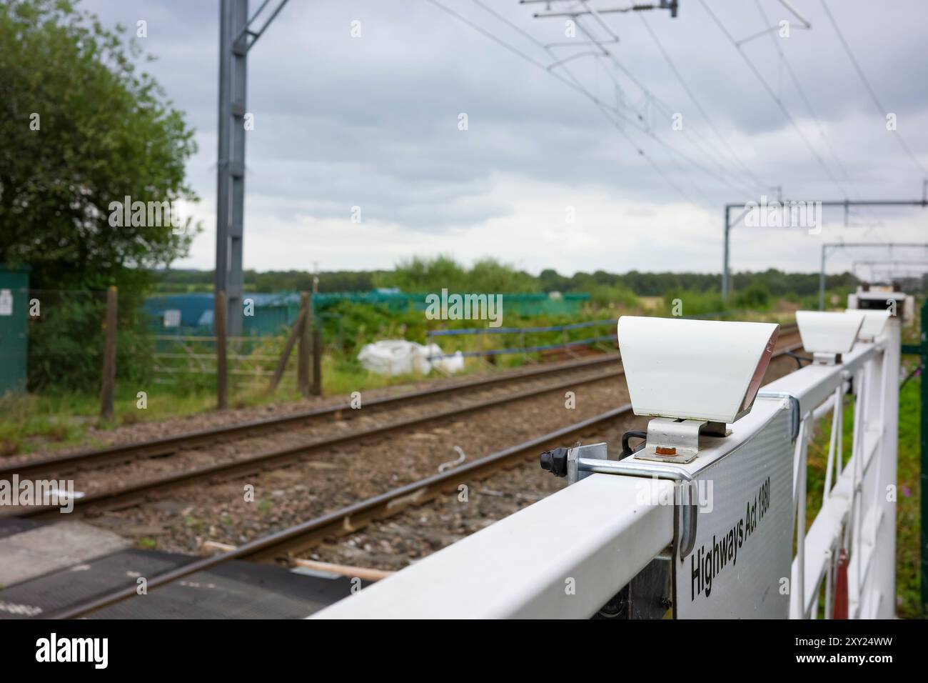 Irlam, Manchester, Großbritannien, 26. August 2024: ländliche Bahnüberquerung mit bewölktem Himmel und grünem Laub. Stockfoto