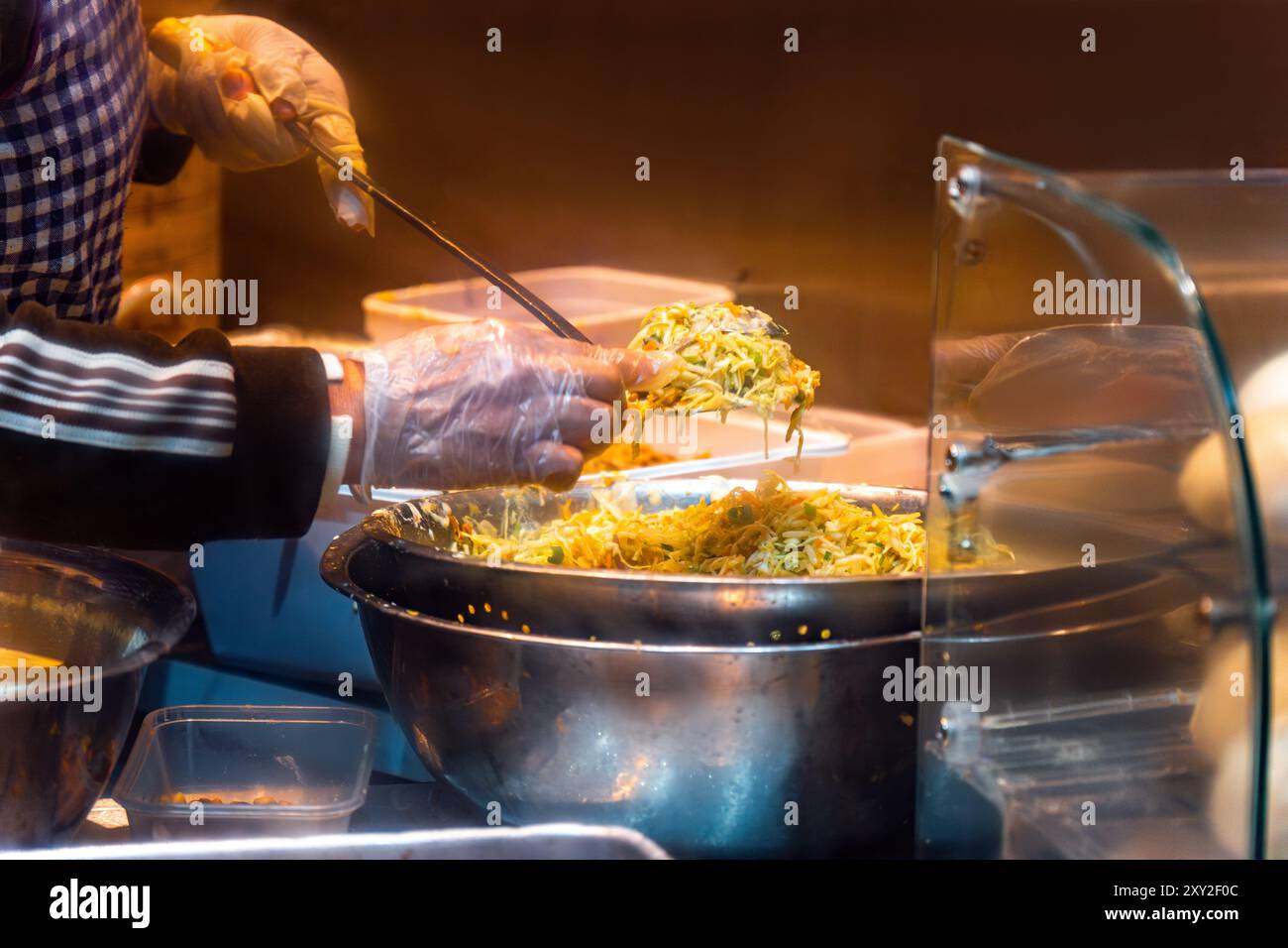 Chinesischer Koch mit Schürze und Kunststoffhandschuhen kocht mit Zutaten in einer Schüssel, um in der Küche eines chinesischen und asiatischen stal zum Mitnehmen Knödel zu machen Stockfoto