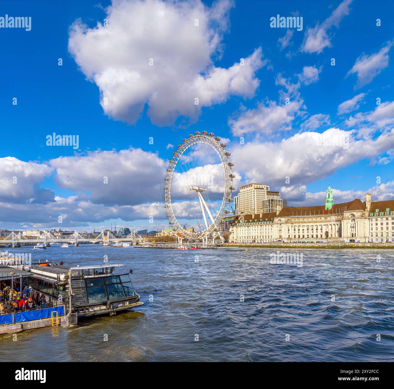 Panoramablick auf die Themse mit Touristen an Bord eines Touristenbootes in einem Fährterminal und dem London Eye Riesenrad im Hintergrund beleuchtet Stockfoto
