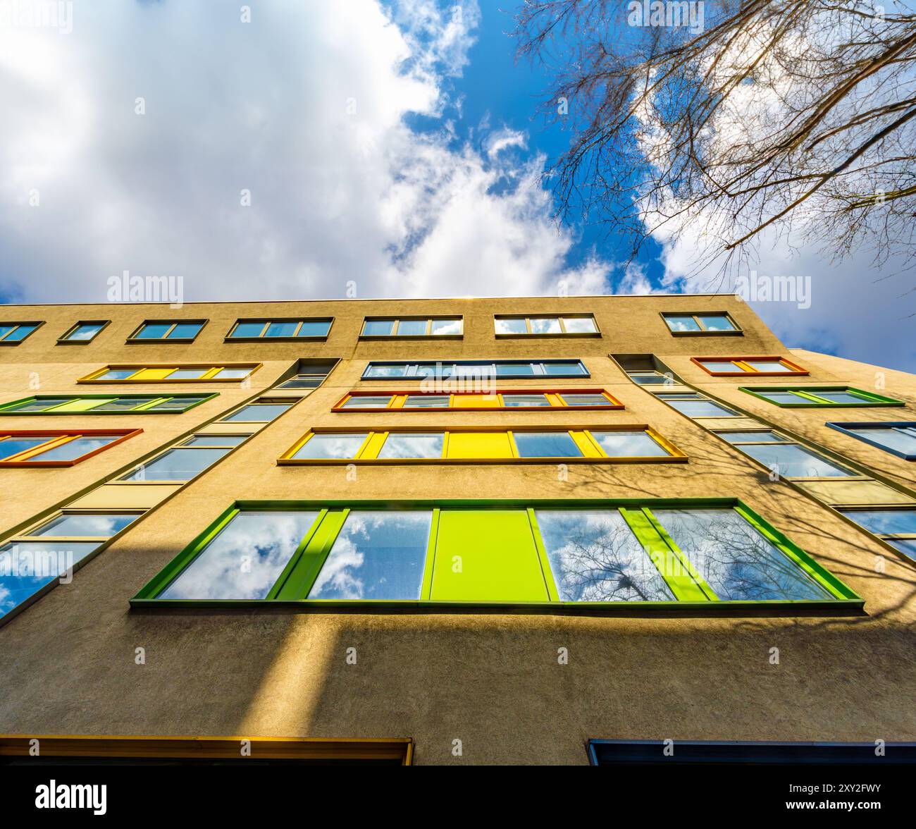 Niedriger Blickwinkel von unten auf bunte Fensterrahmen in einem sonnendurchfluteten Londoner Bürogebäude unter blauem Himmel mit weißen Wolken. Stockfoto